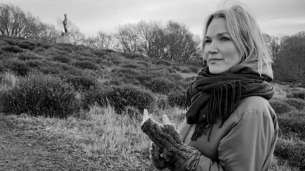 Photographer Frida Gregersen standing with heather in the background. Black and white