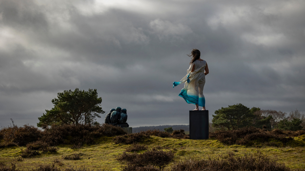 Woman standing with her back turned in a windblown dress on a pedestal in the heather