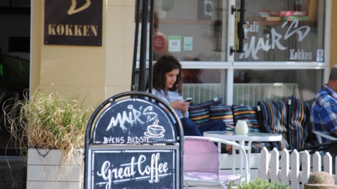 cafe-skilt fra cafe mairs. I baggrunden sidder en kvinde foran cafeen.