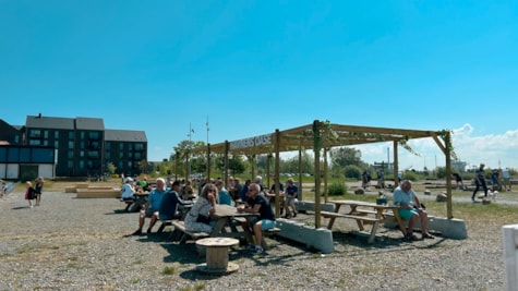 Mennesker sidder og slapper af under en pergola i grønne omgivelser.