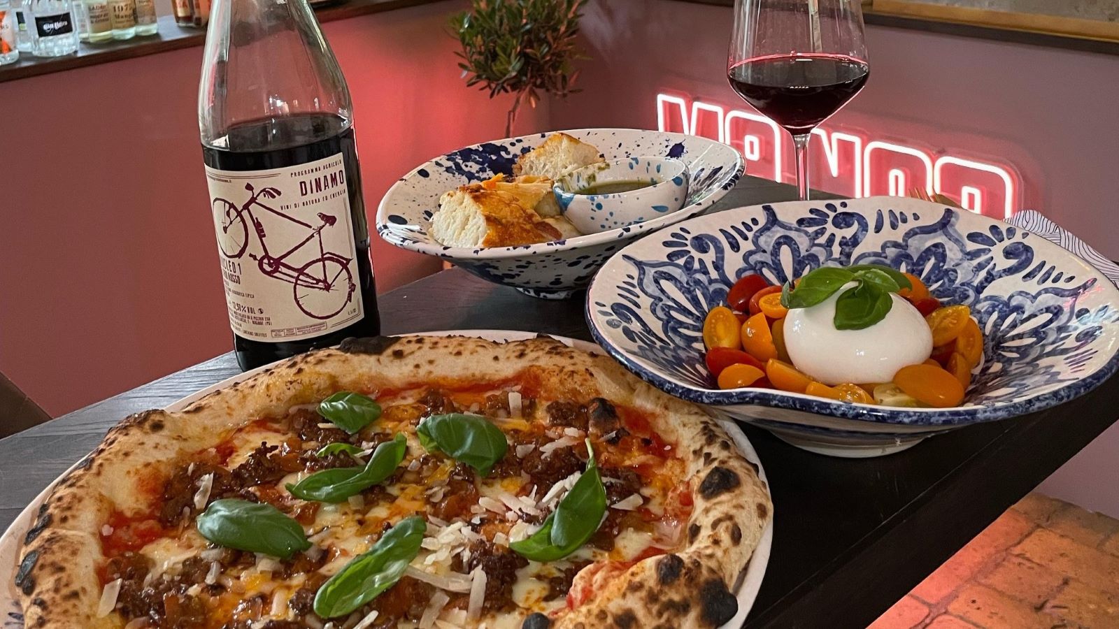 Tisch mit Pizza, Nudelgericht und einer Flasche Wein in einem Restaurant.