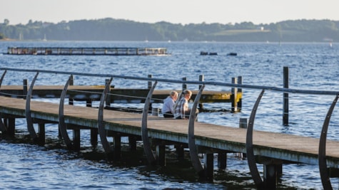 To piger sidder på badebro ved vandet i Skærbæk Strandpark.