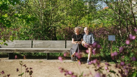 Par sidder på bænk i Søndervold Naturpark og lytter til et kunstværk.