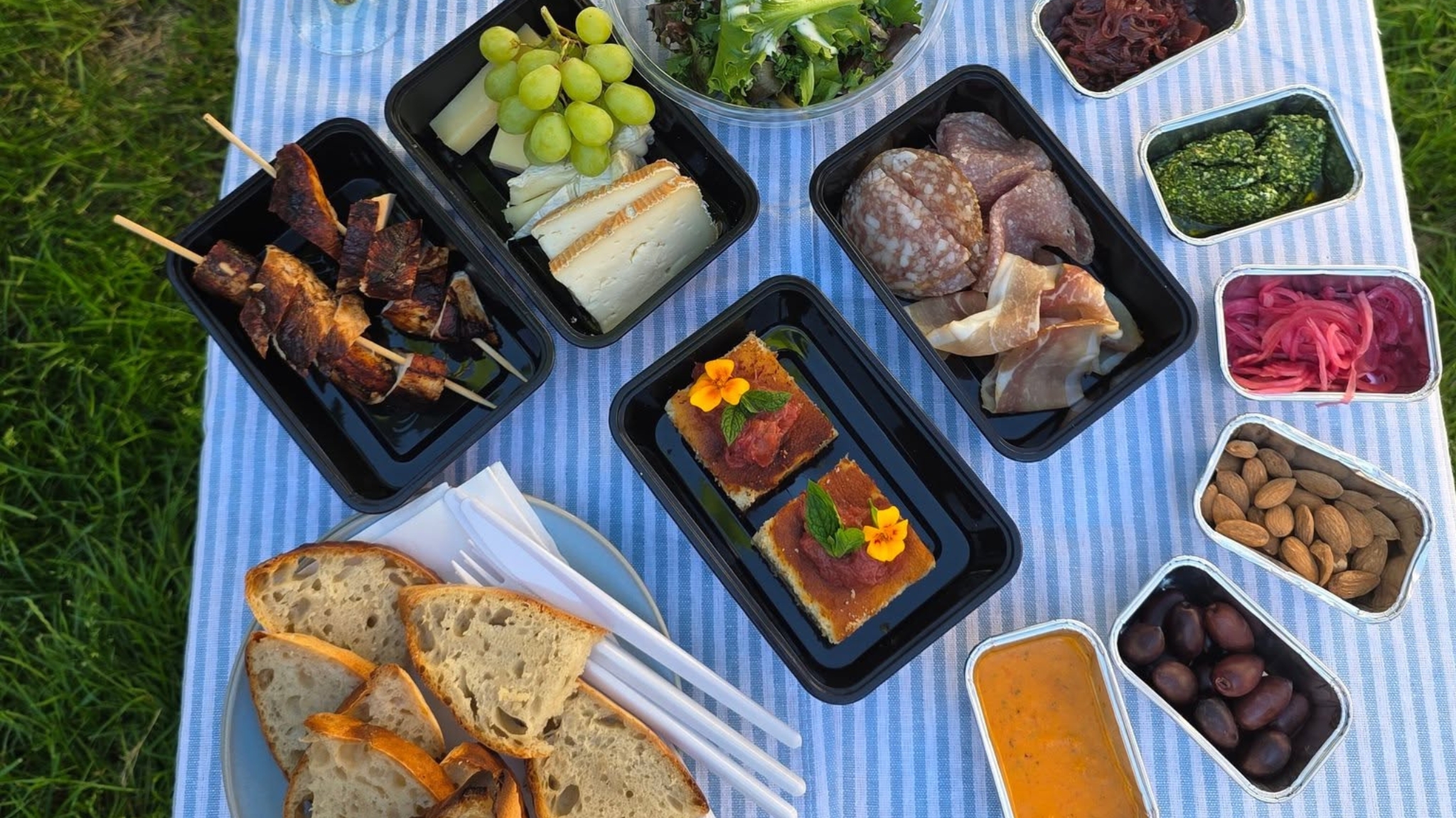 Contents of Café Himmelblå's picnic basket with charcuterie, cheeses, salad, chicken skewers, homemade bread, dips and cake.
