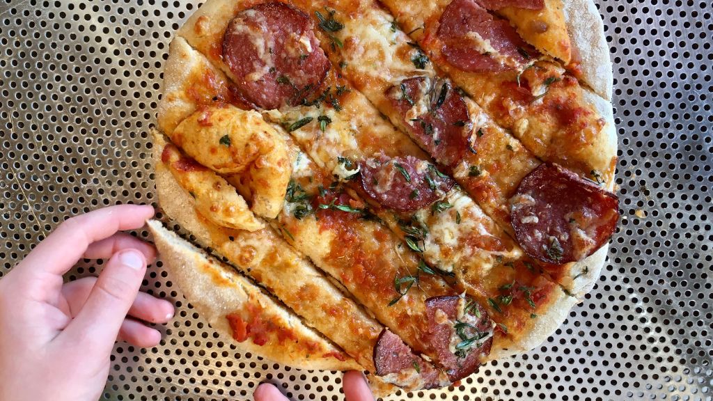 pizza ligger på bageplade og en hånd tager et stykke pizza