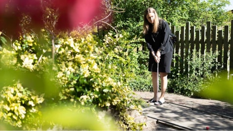 Молода жінка в чорному одязі грає в міні-гольф