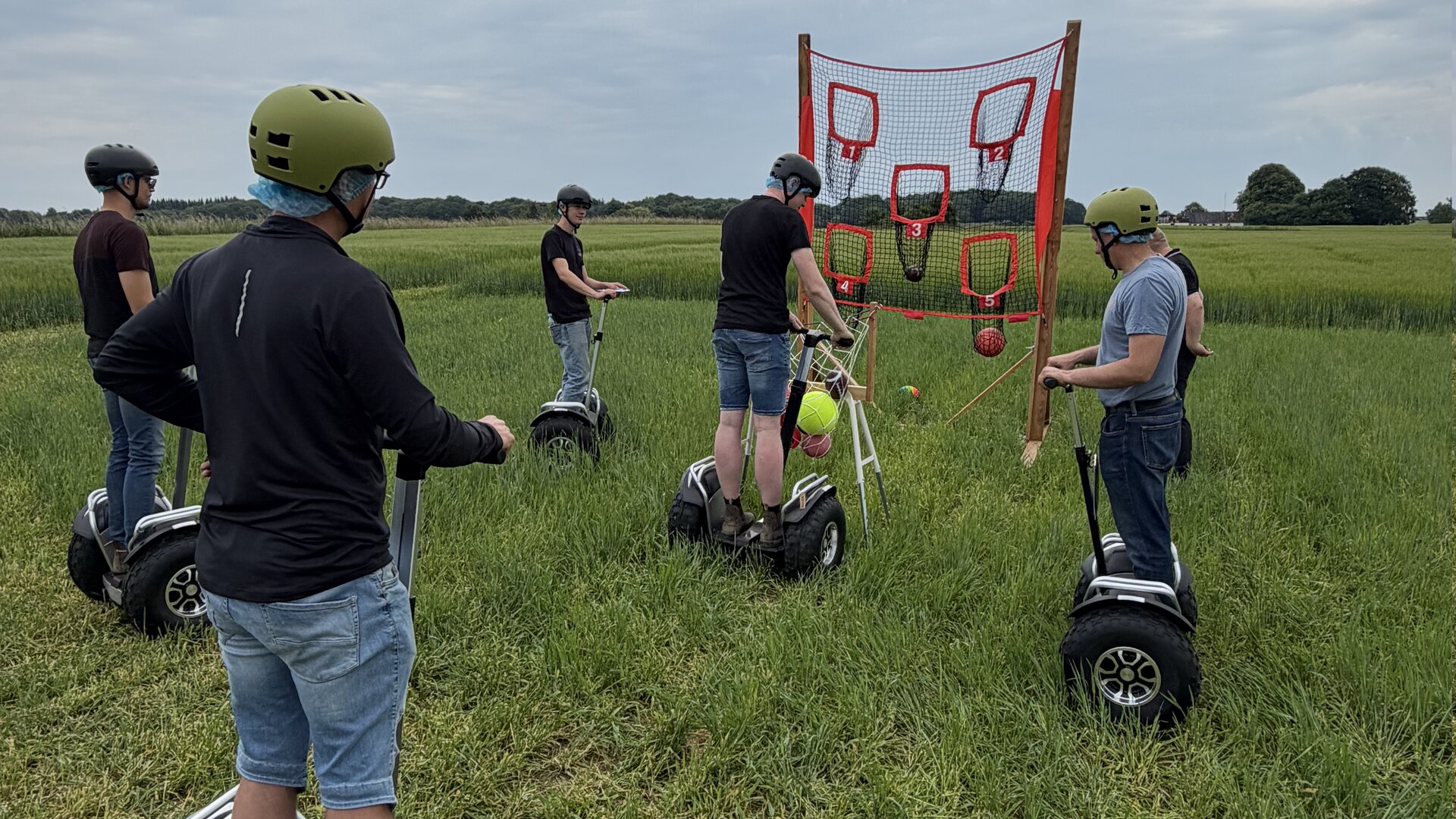 Instruktør i grøn trøje introducerer fem deltagere med hjelm på Segway-terrængående i et grønt naturområde.