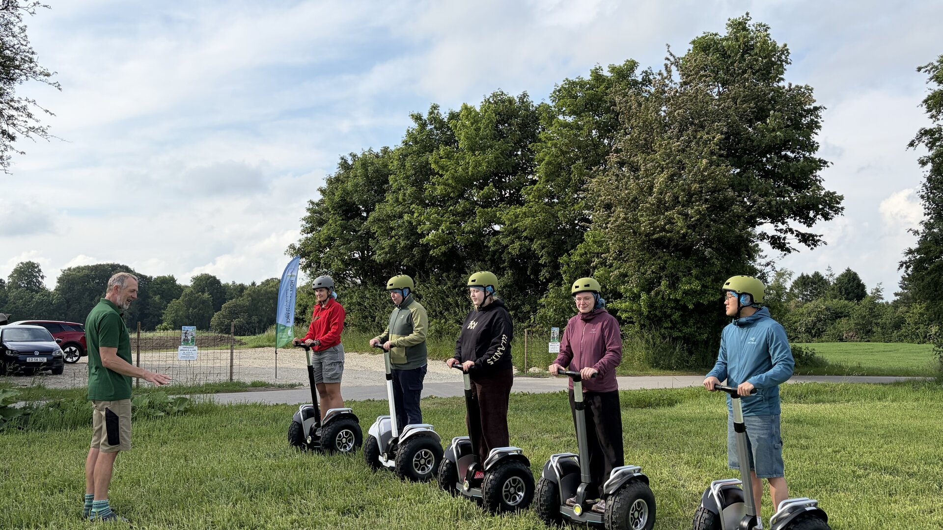 Instruktør i grøn trøje introducerer fem deltagere med hjelm på Segway-terrængående i et grønt naturområde.