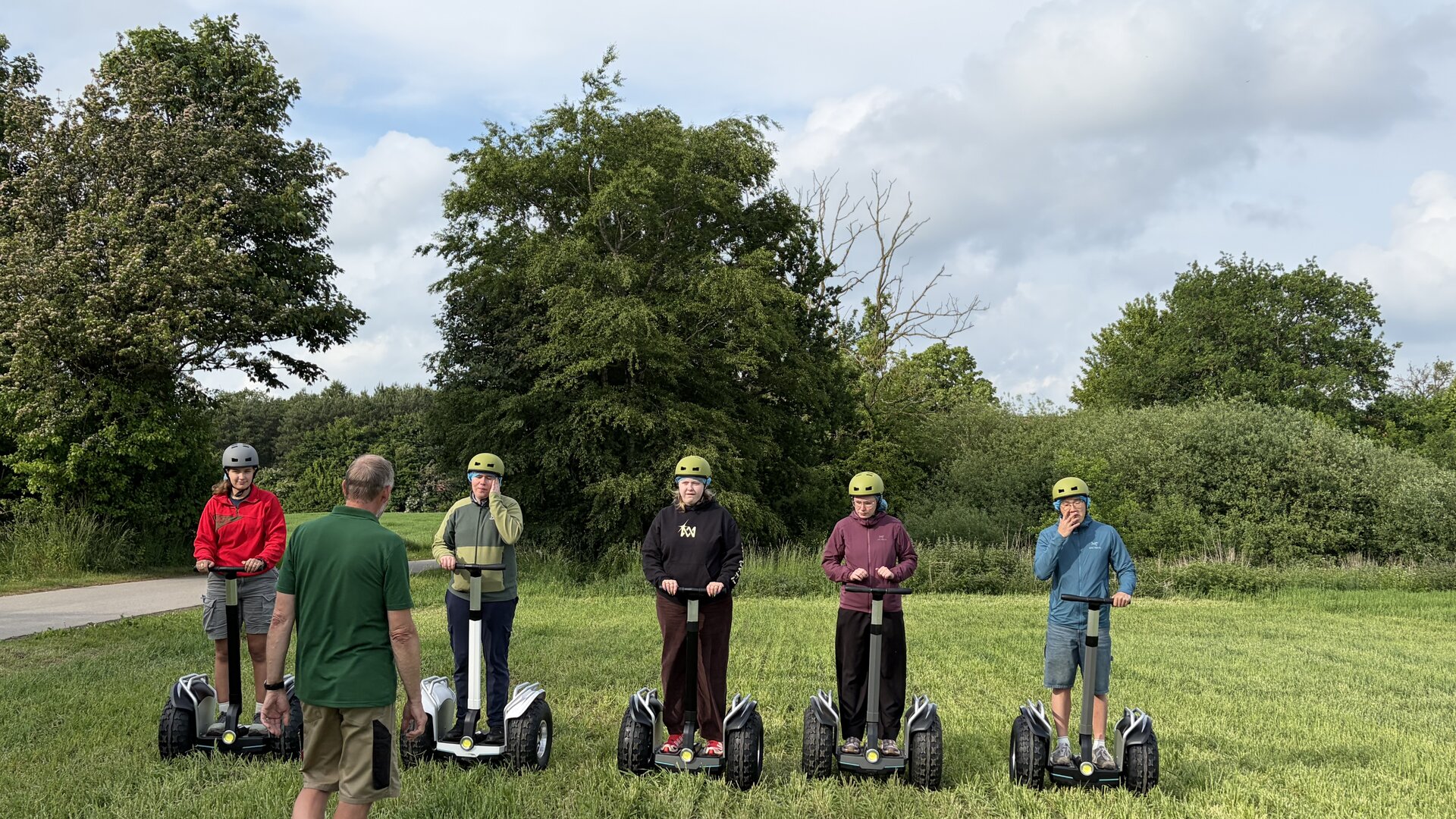 Instruktør i grøn trøje introducerer fem deltagere med hjelm på Segway-terrængående i et grønt naturområde.
