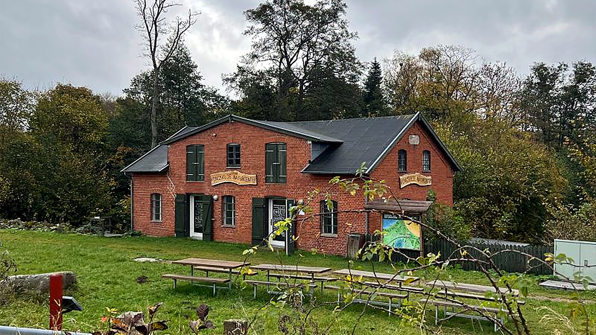 Kongskilde Naturcenter — rødstensbygning med bænke og borde på græsplænen, omgivet af skov.