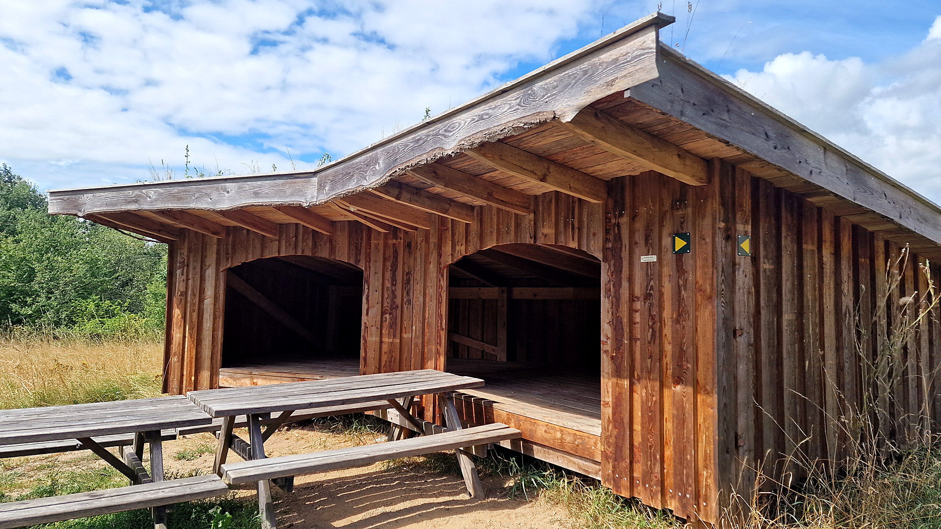 Wooden shelter with a green roof, two open sleeping bays and a picnic table at Skellingsted outdoor area.