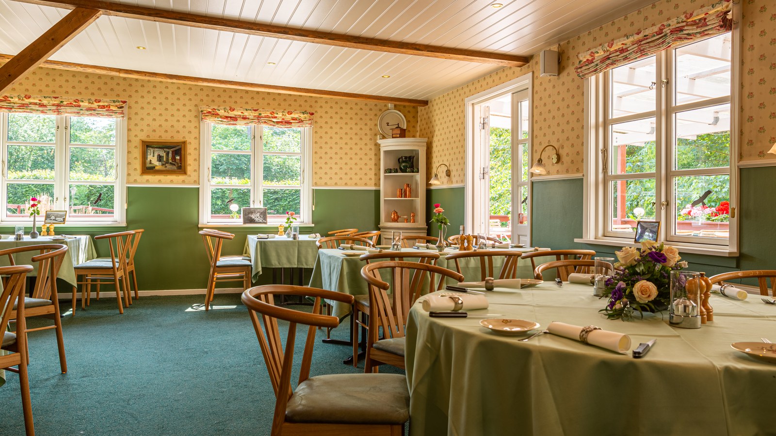 he restaurant at Bromølle Kro with laid tables, green wainscoting, floral wallpaper and views of the greenery.
