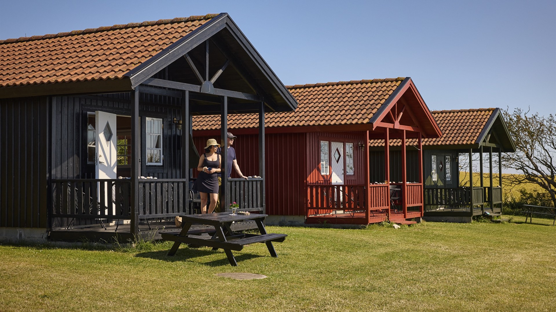 Drei farbige Holzhütten mit überdachter Terrasse auf dem Urhøj Camping bei Store Fuglede
