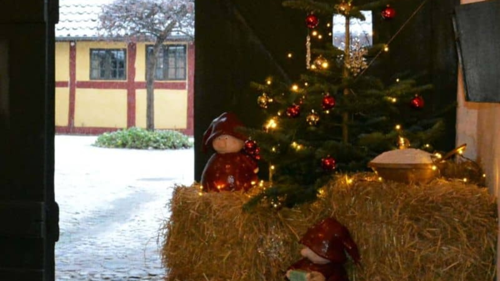 Christmas tree with lights and elves on straw bales in the gateway of Sorø Museum with snow in the courtyard