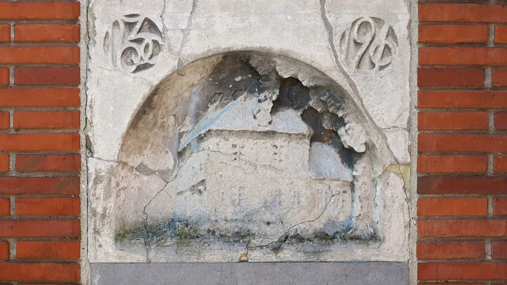 Sandstenstavlen på Langegade 6. Tavlen er præget af tidens tand, og inskriptionerne er utydelige.