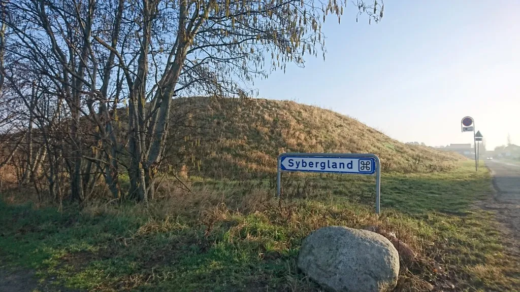 Sign pointing towards Sybergland, along with trees and a hill.