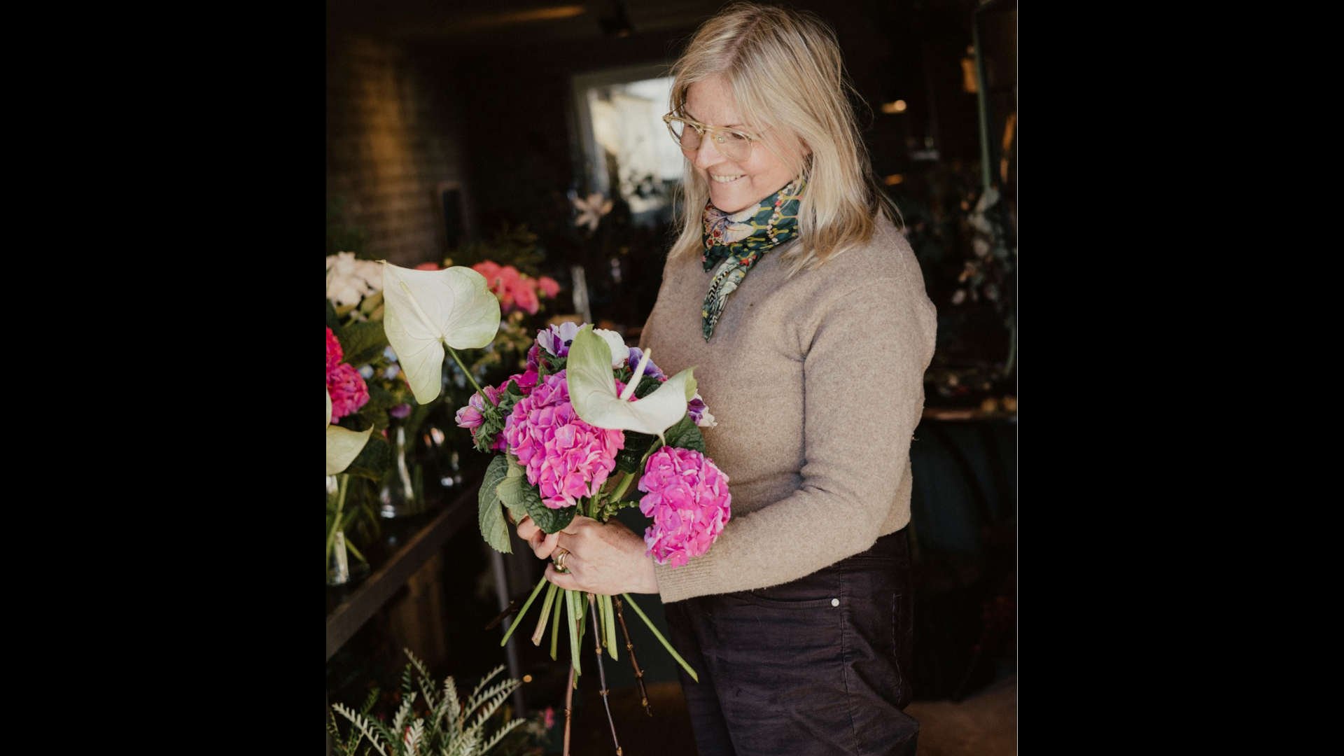 Vibeke i cowboybukser og sandfarvet trøje med hvide og lyserøde blomster