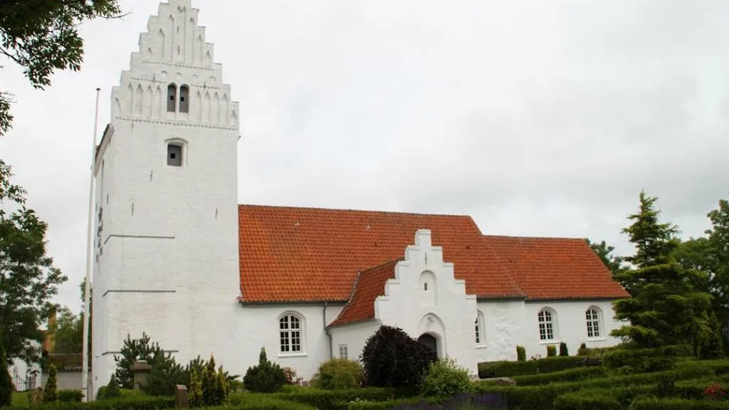 Photo of Revninge Kirke, which is white with a red roof.