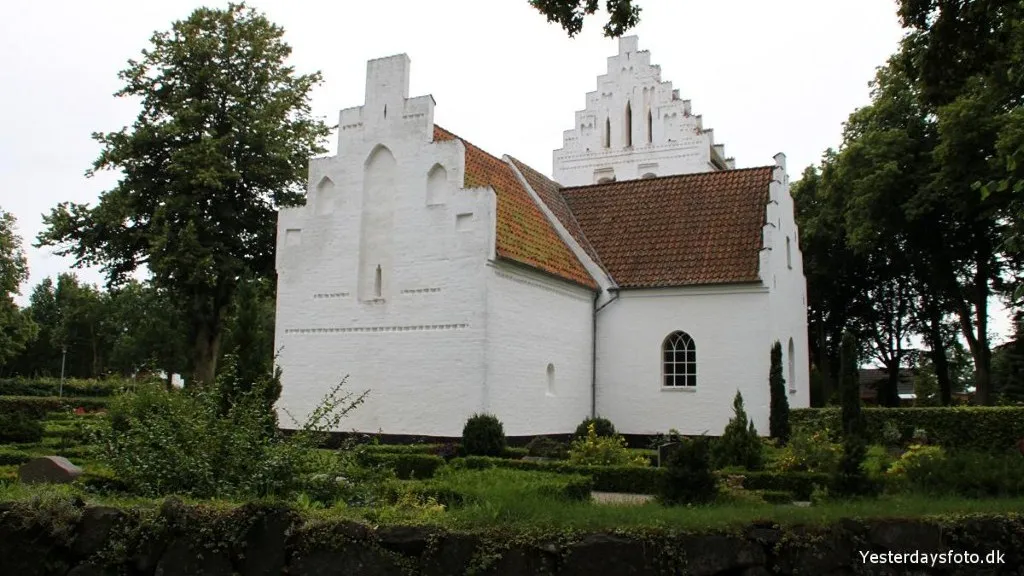 Et foto af Birkende Kirke, en hvid bygning med et rødt tegltag, omgivet af træer og grønne områder i Kerteminde Kommune på Fyn.