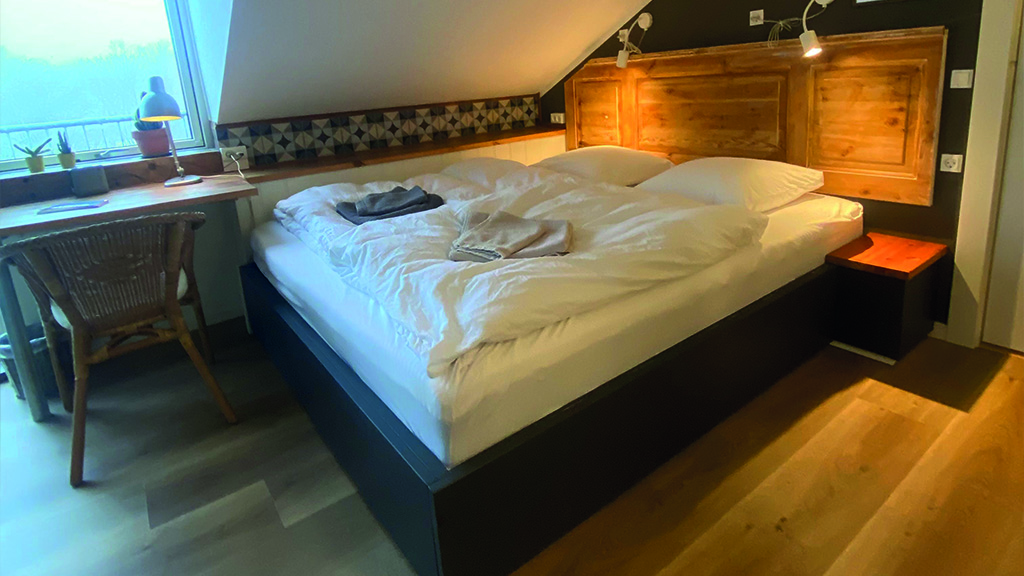 Zimmer in Samsted mit Doppelbett und kleinem Schreibtisch. Über dem Bett befindet sich eine schräge Wand.