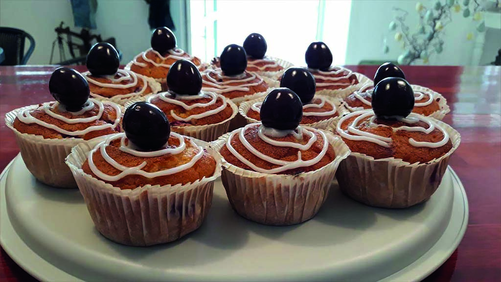 Kirsebærmuffins på hvidt fad. Muffins har en hvid glasurspiral på topppen og et kirsebær