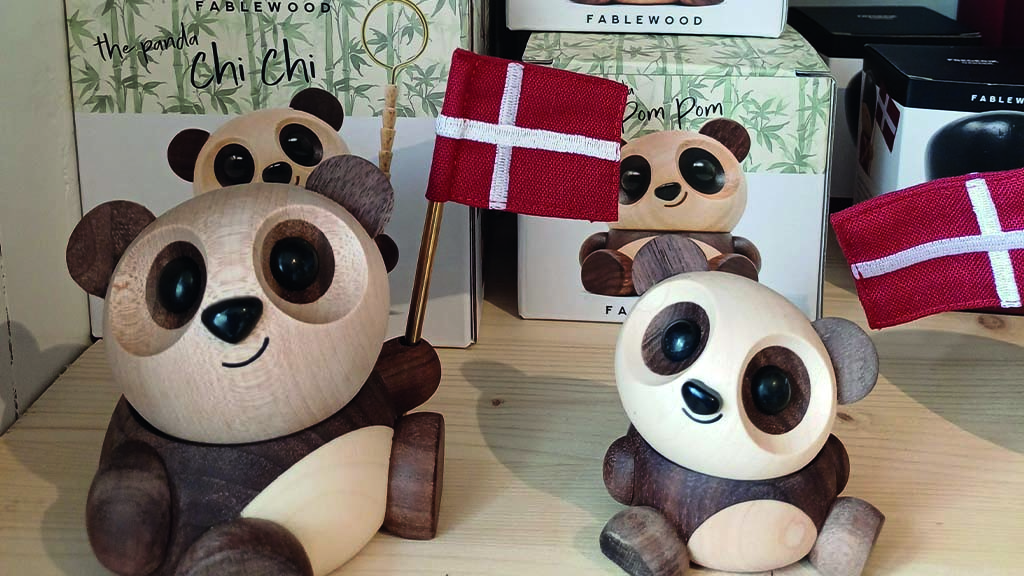 Two wooden pandas sitting on a table. The pandas are two different sizes – the larger one is holding a flag in its hand.