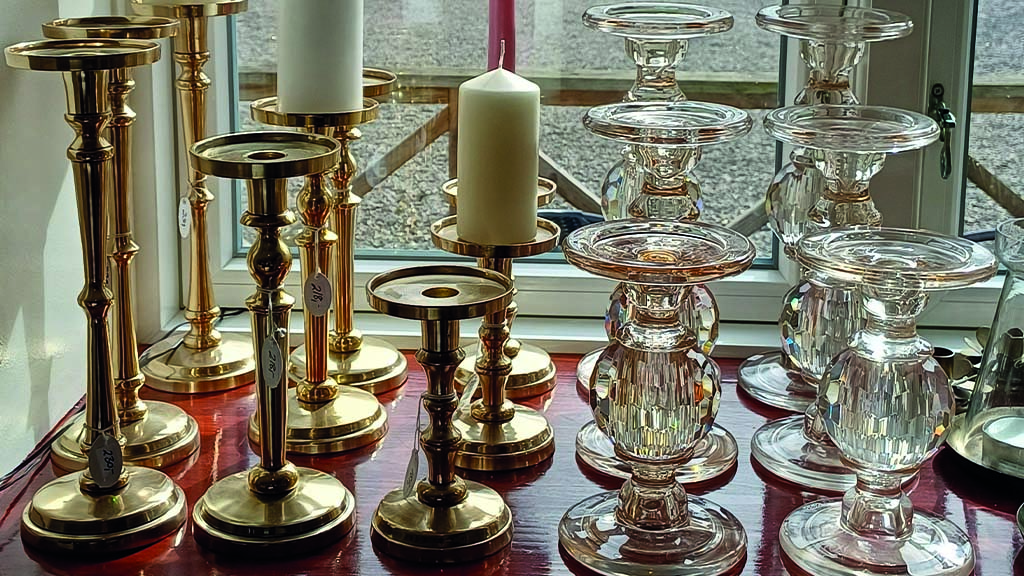 Brass and glass candlesticks in the shop window. Some of the holders are for pillar candles and others for taper candles.