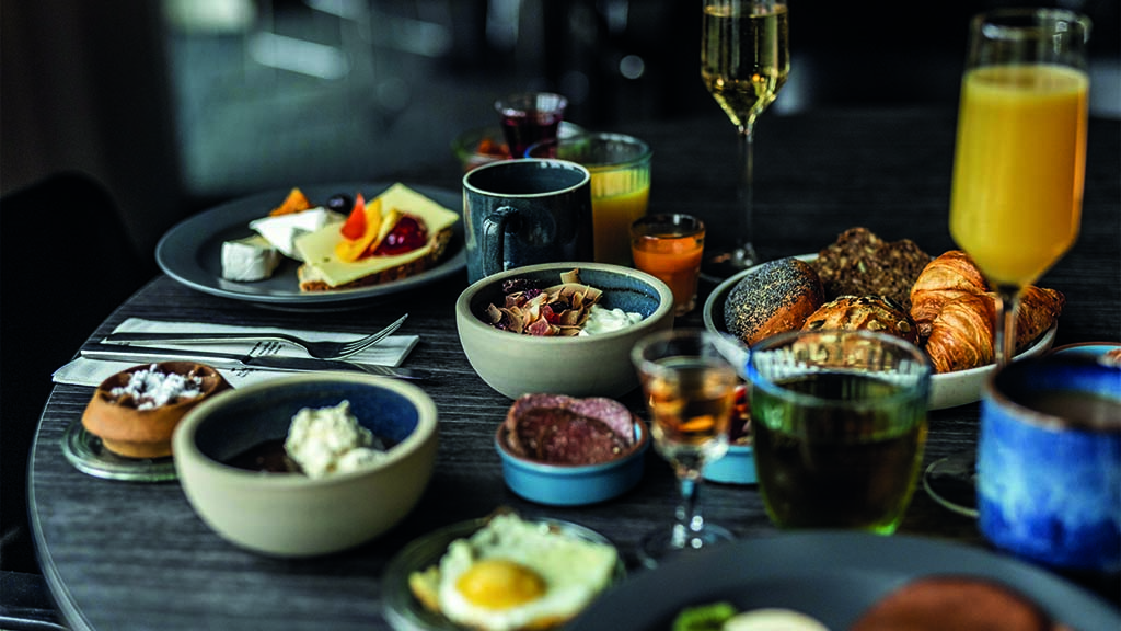 Breakfast at Comwell Middelfart. There are several small bowls with items including bread rolls, eggs and cold cuts. There is juice in champagne glasses and coffee in cups.