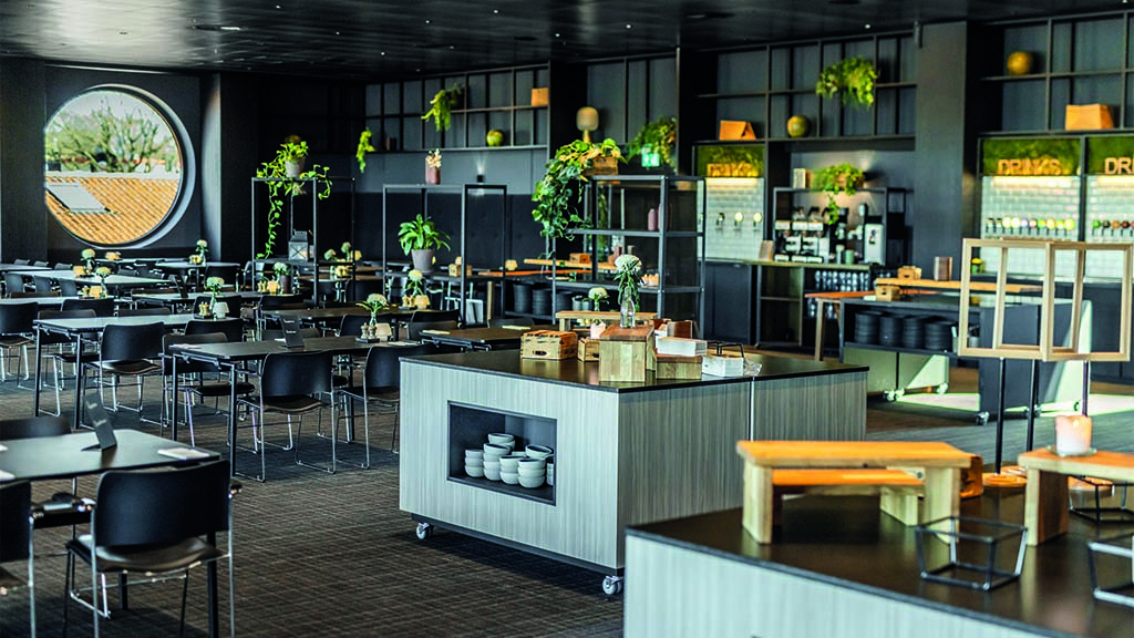The restaurant at Comwell has kitchen islands for the buffet. Each table seats approximately 6 people. The room has a modern, dark interior.