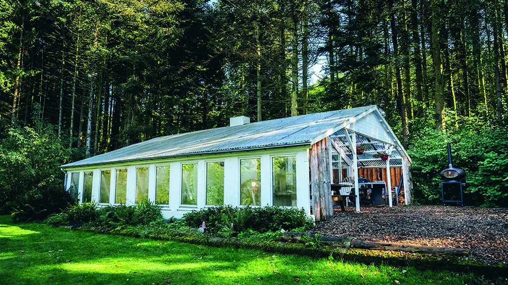 Orangerie aus weißem Holz mit großen Fenstern. Dahinter befindet sich ein Wald.