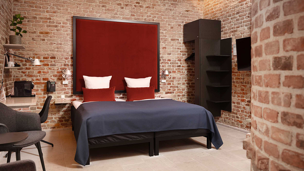 A room at Hindsgavl. The walls are raw red brick. A large double bed with a red headboard and blue bedding.