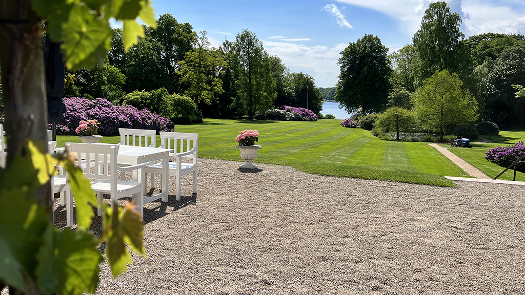 The park at Hindsgavl on a summer's day. A white garden table and chairs on gravel in front of a large lawn.