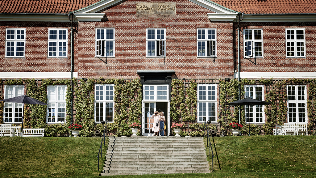 The entrance to Hindsgavl Castle. A grand staircase leads up to the entrance. The lower part of the wall is covered with climbing plants.