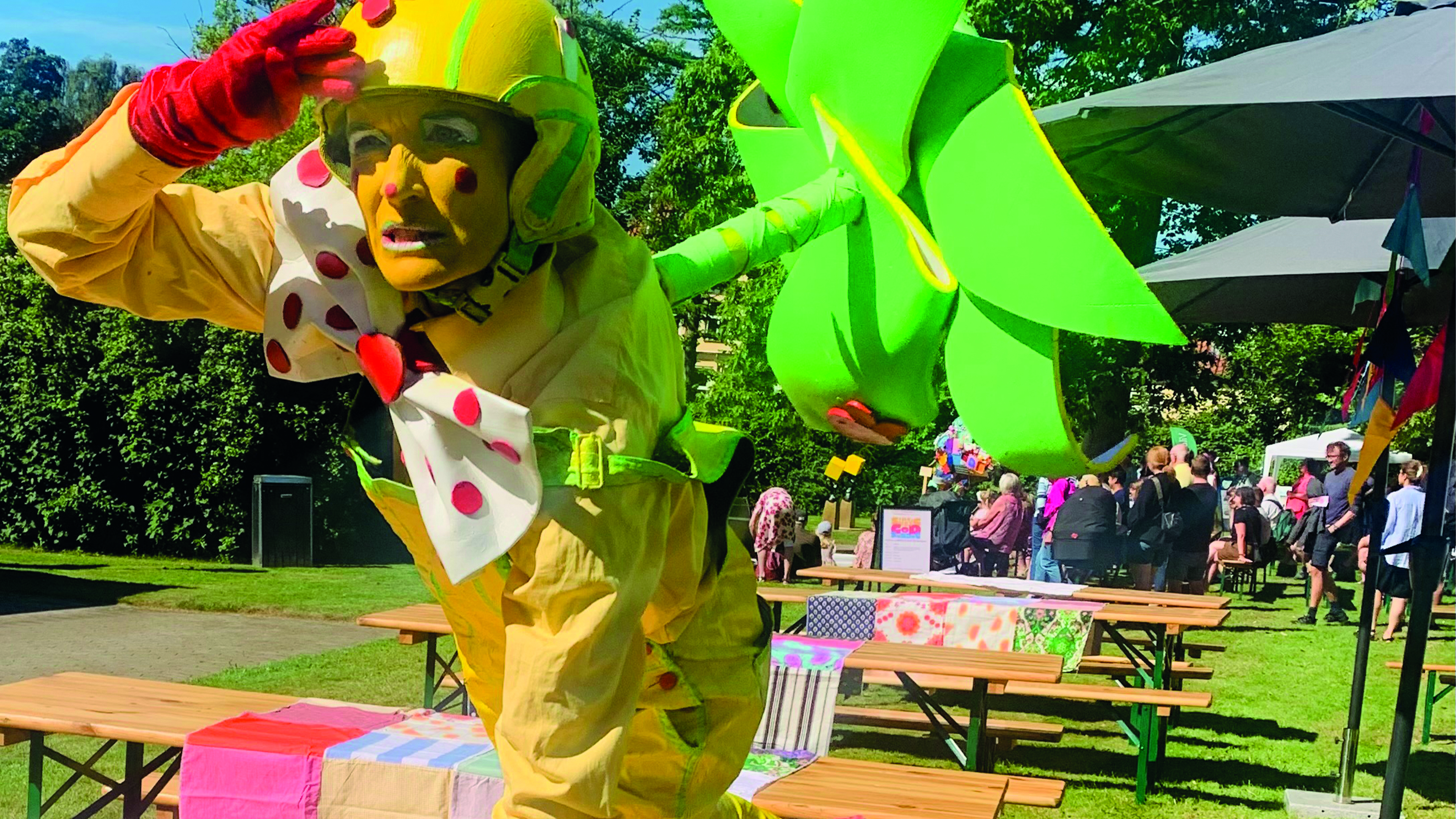 A lady dressed in a yellow costume and painted yellow on her face. On her back she has a green propeller. She is scouting for something.