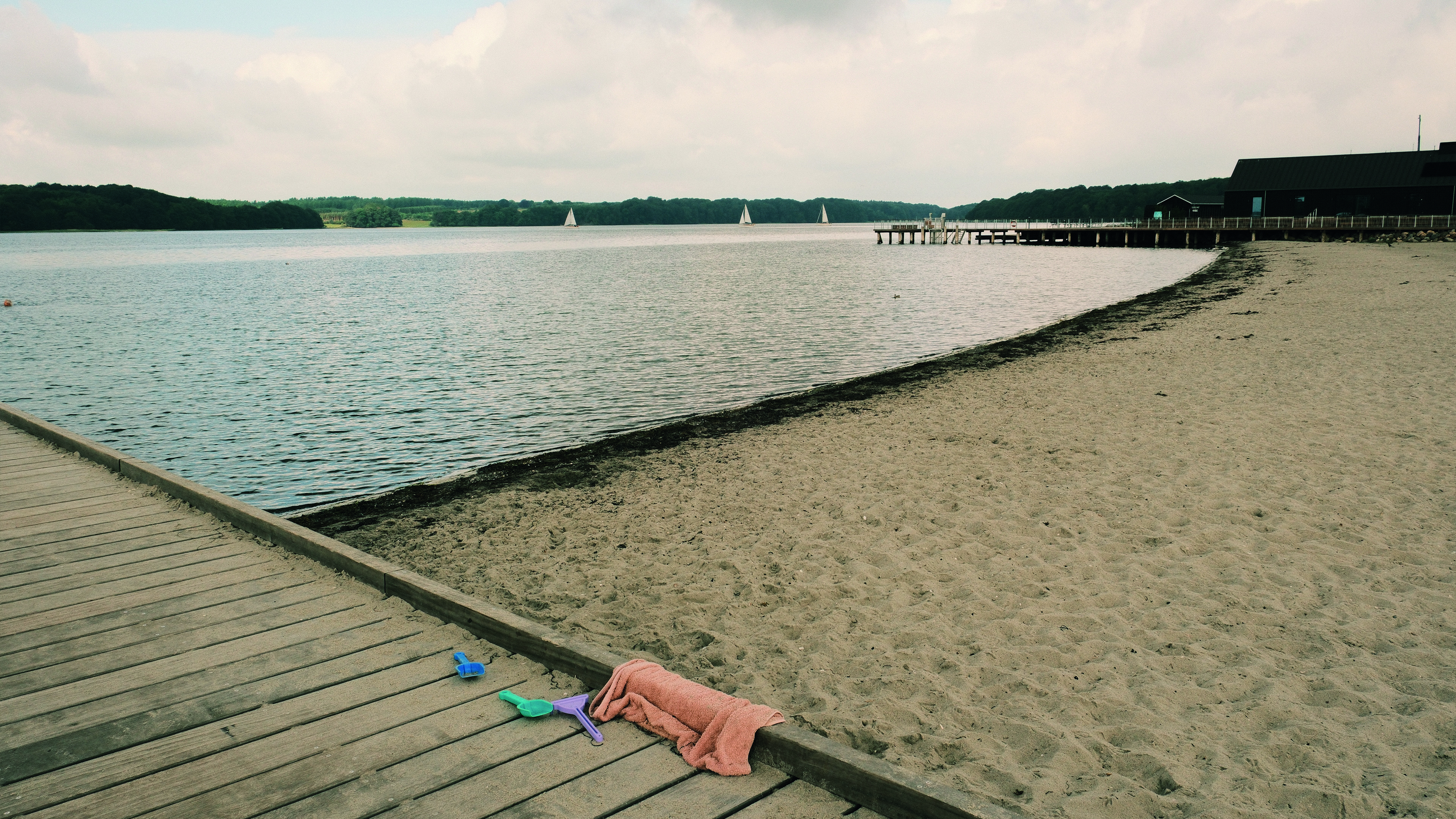 The beach at Middelfart Marina. A child has forgotten a towel and plastic shovels.