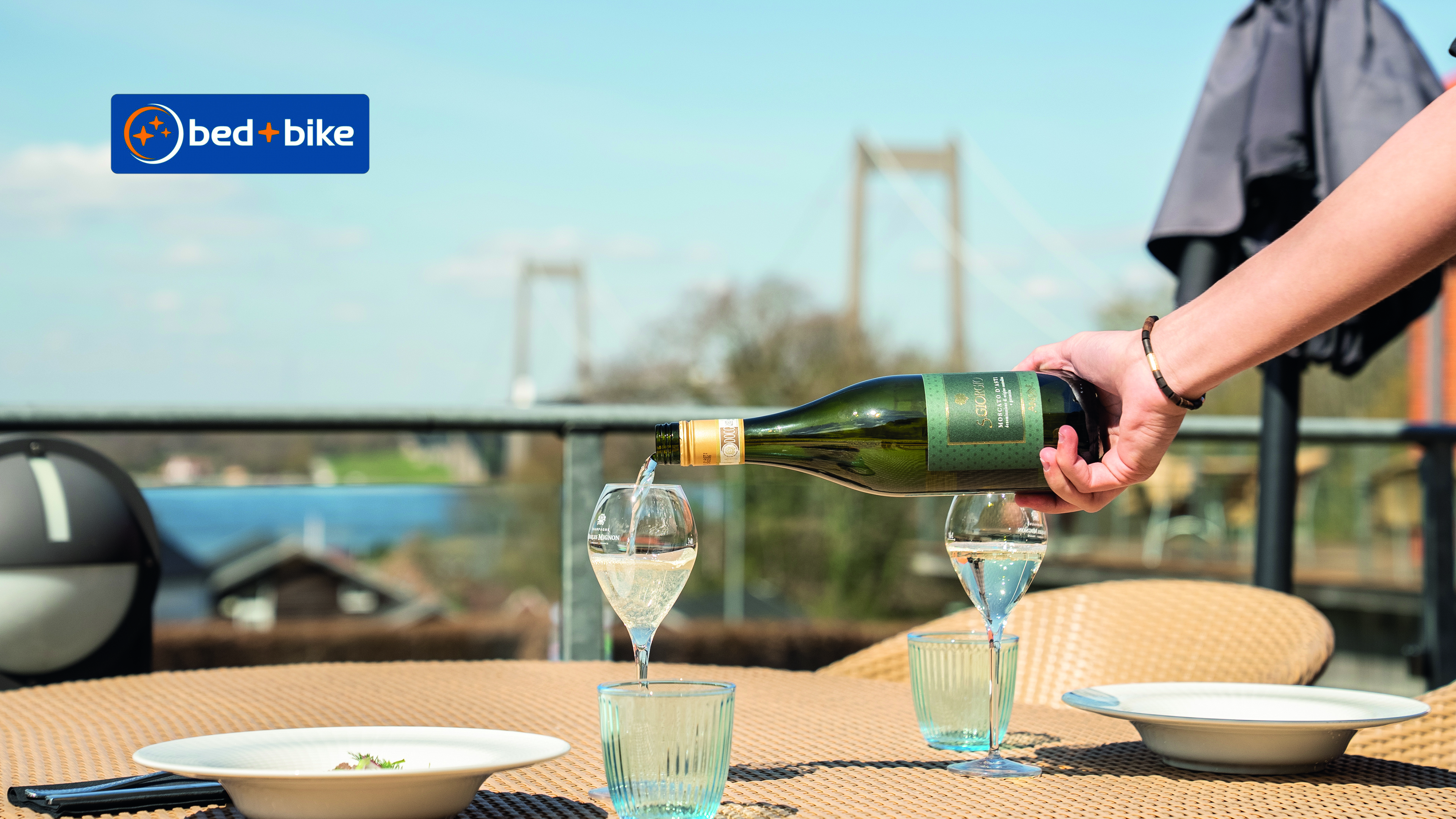 Eine Frau schenkt Weißwein in ein Glas ein. Im Hintergrund ist die New Little Belt Bridge zu sehen.