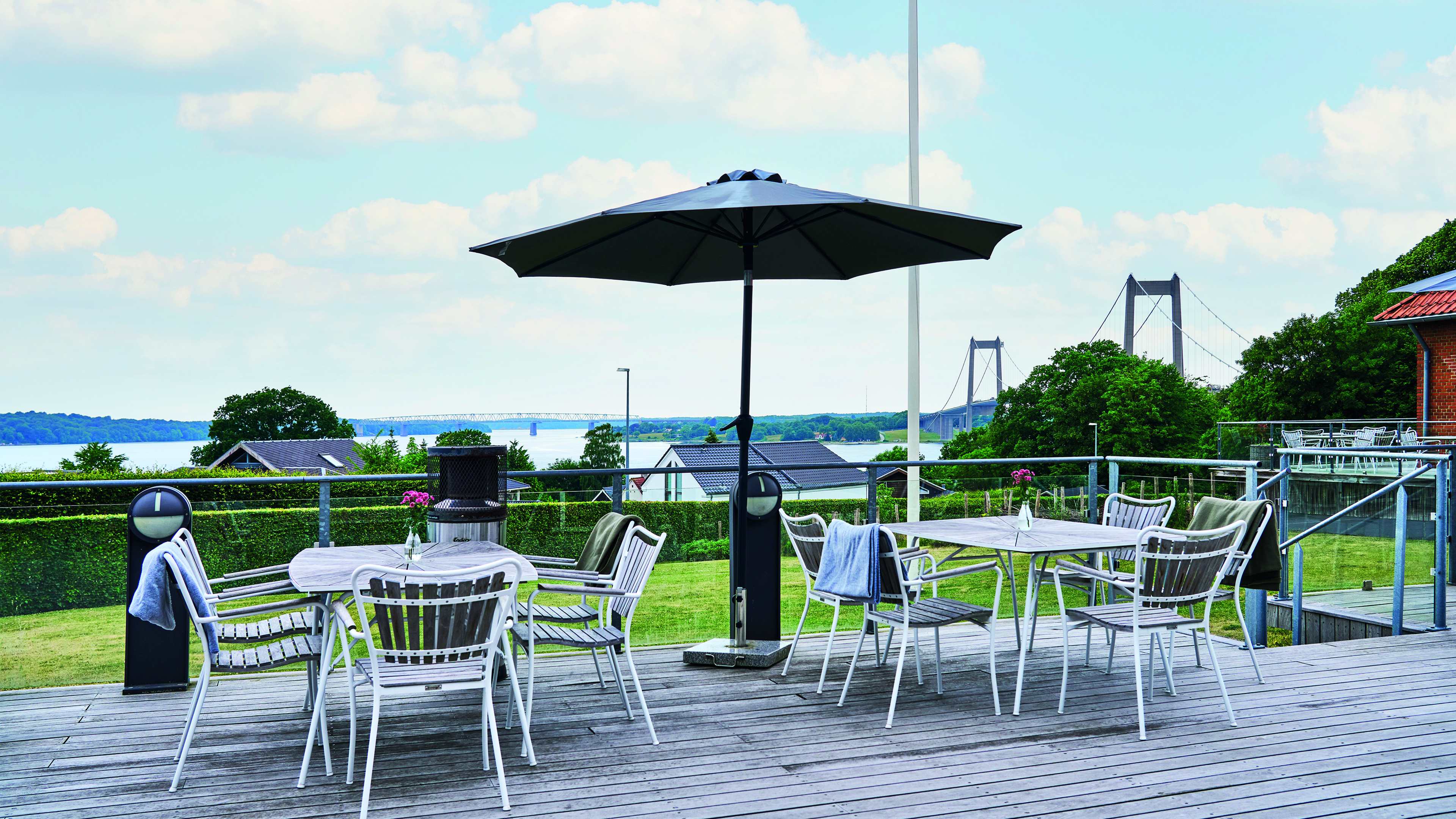 Terrasse mit Tischen und Stühlen. Im Hintergrund ist die Neue Kleine Belt Brücke zu sehen.
