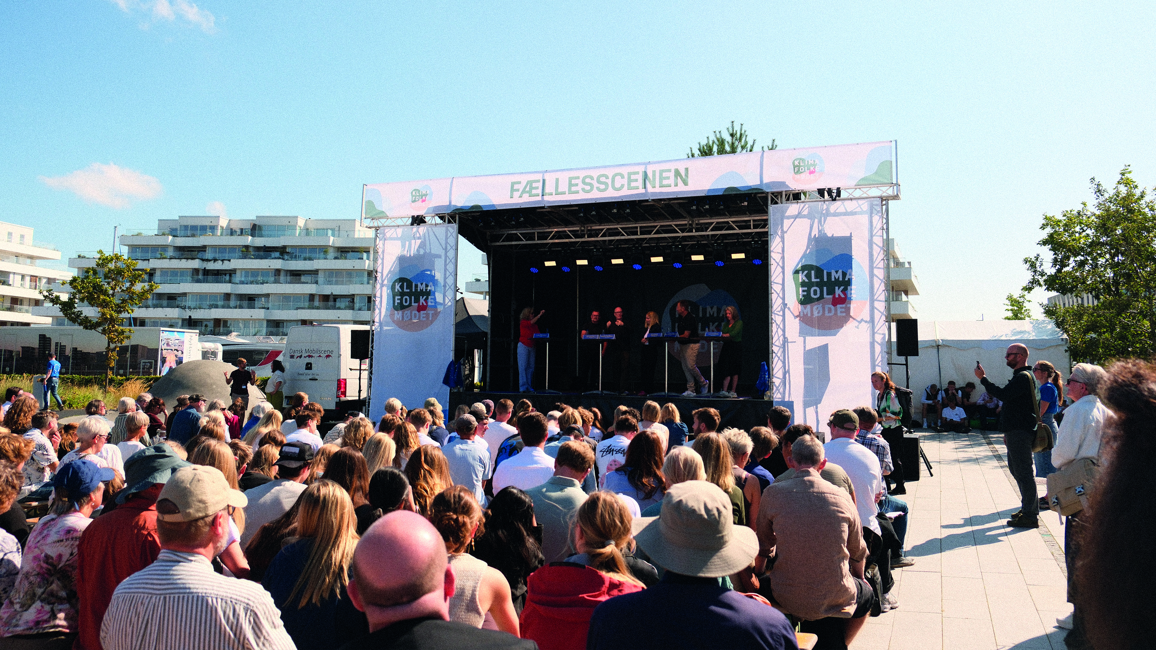 Det er en sommerdag, en stor scene med 4 mennesker debatterer, foran sidder en masse mennesker og lytter