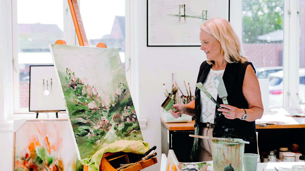 Gitte Ladefoged paints pictures of a meadow with flowers. In the background, there are other pictures.