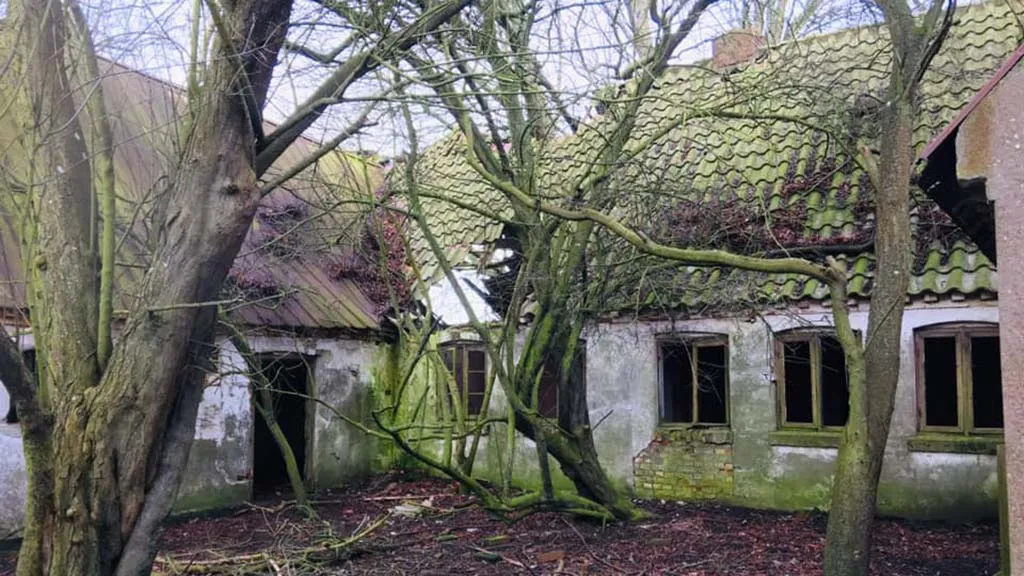 En gårdbygning er ved at blive til en ruin under træerne på Dræet
