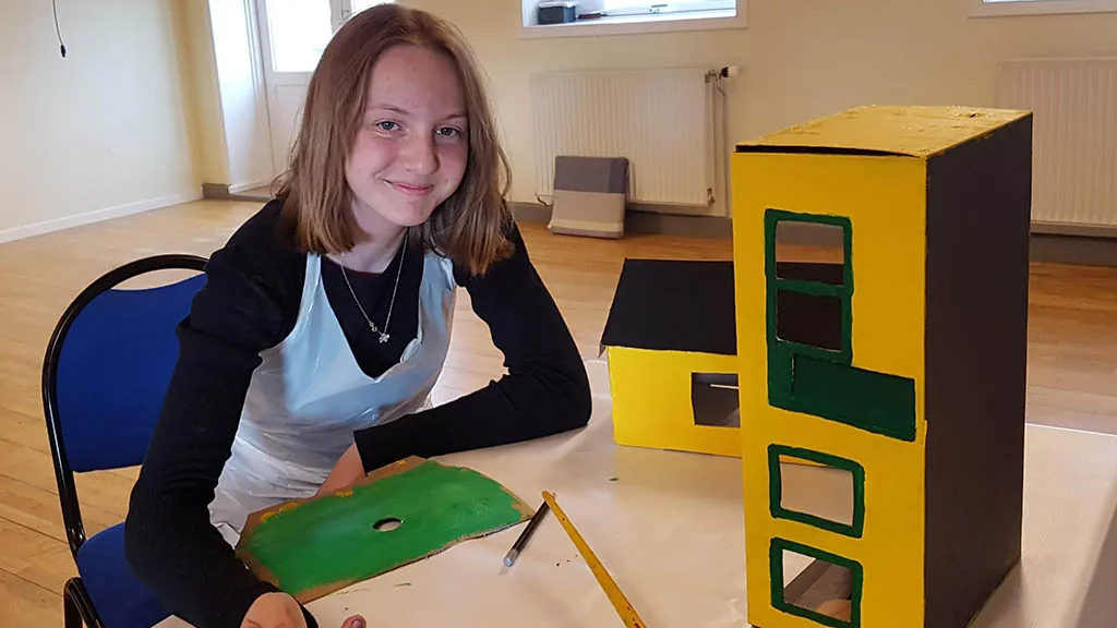 A girl paints the grass for a cardboard house