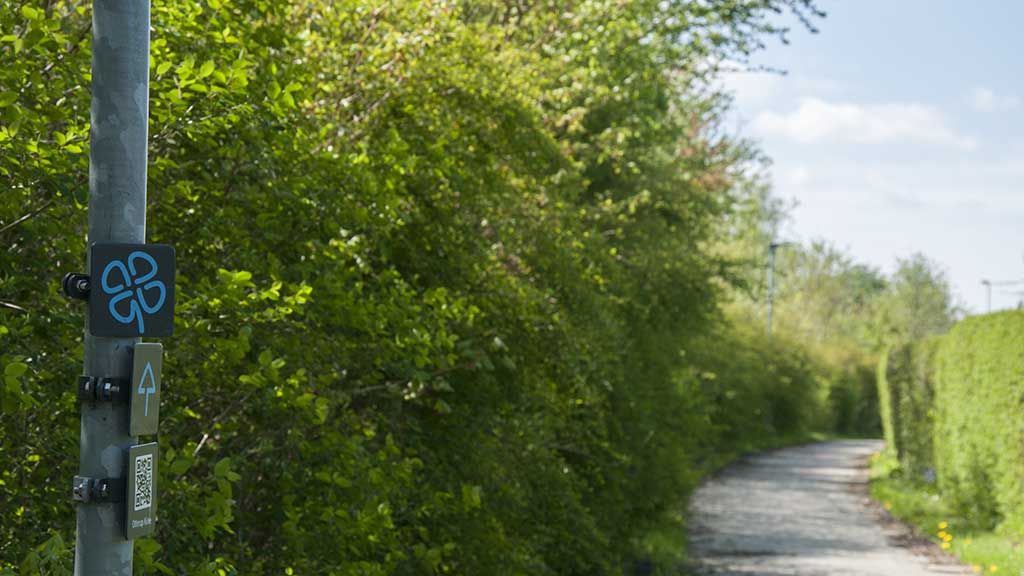 The clover leaf sign at the path in Otterup surrounded by green bushes