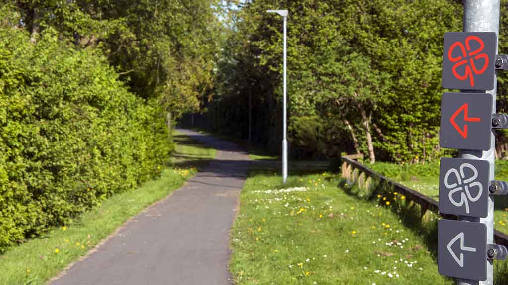 Signs for the red clover leaf route from Søndersø on a path surrounded by green bushes and trees