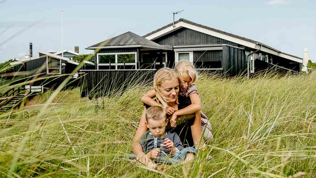 Mutter und Kinder vor einem schwarzen Sommerhaus aus Holz im Sommer auf Nordfünen