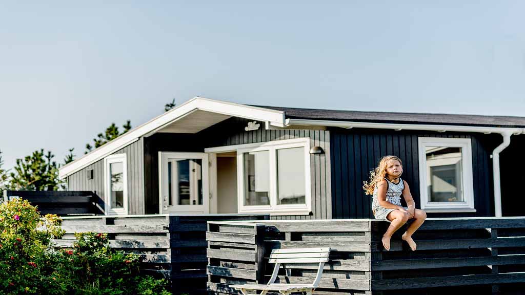 Kleines Mädchen mit blonden Haaren sitzt auf der Terrassenmauer im Sommerhaus auf Nordfyn