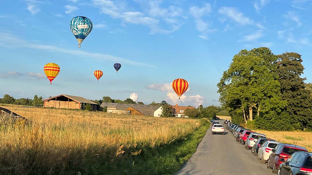 Ballons in der Luft über dem Feld und der Straße mit Autos für den DreamBalloon Cup