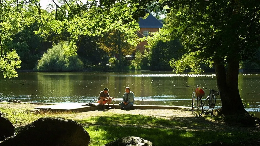 Two cyclists take a break by the lake shore with a view of Langesø Castle