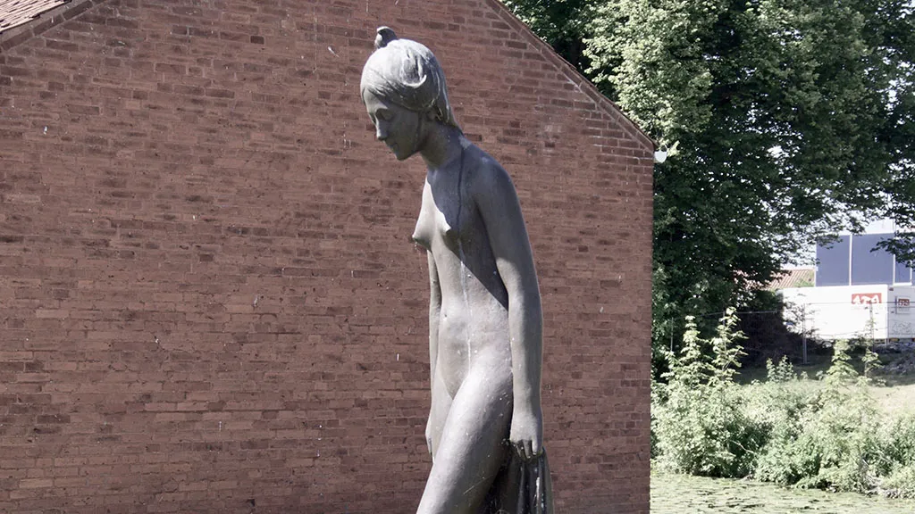 På græsset ved Nyborg bibliotek og med Nyborg slot som bagtæppe står en bronzeskulptur af en ung spinkel kvinde.
