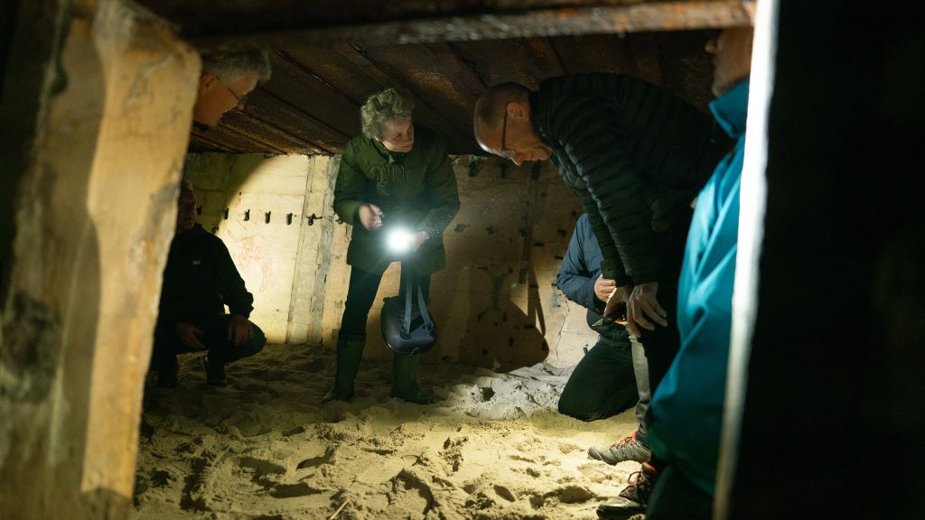En gruppe mennesker på en rundvisning med lommelygter i en mørk bunker.