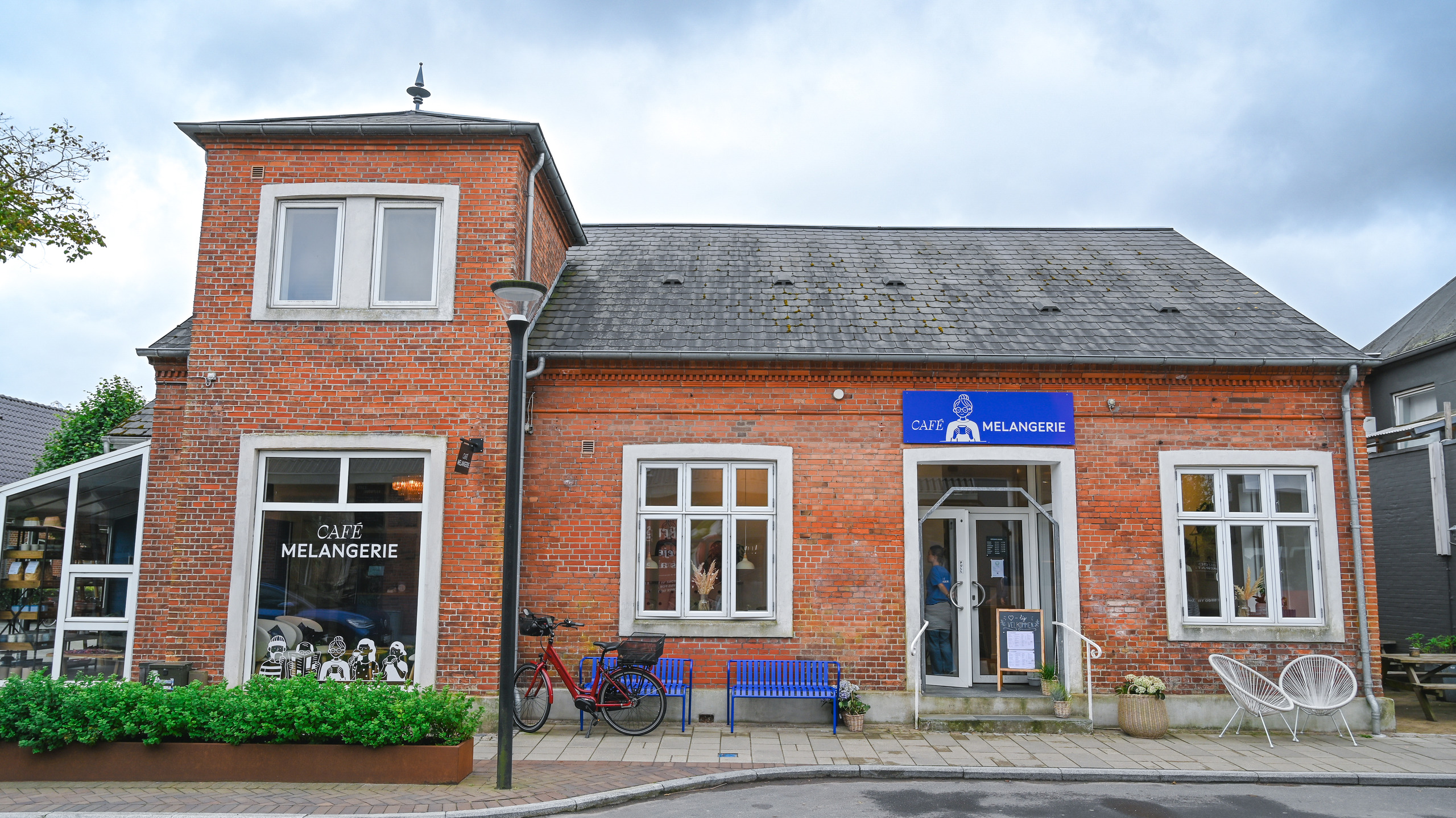 An inviting red-brick house with a blue sign reading "Café Melangeri".